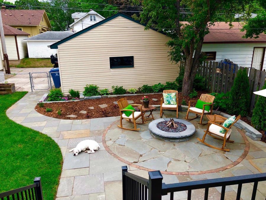 Backyard patio with rocking chairs around a fire pit, surrounded by garden beds