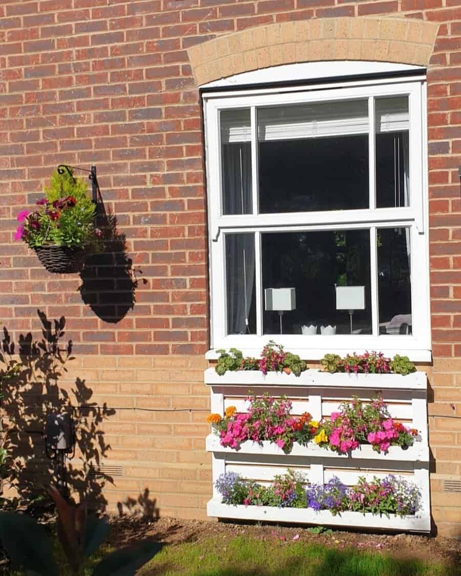 Outdoor pallet flower box in front of a window on a brick wall