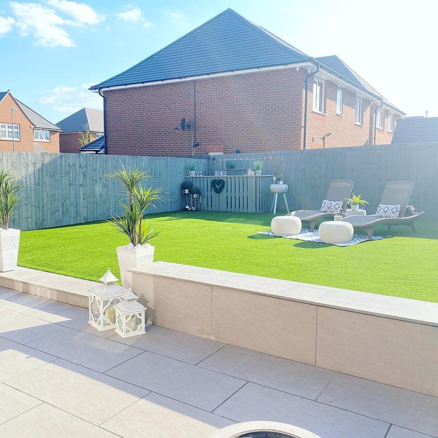 Modern backyard with artificial grass, cozy lounge chairs, stylish planters, and a clean patio area for relaxing under sunny skies