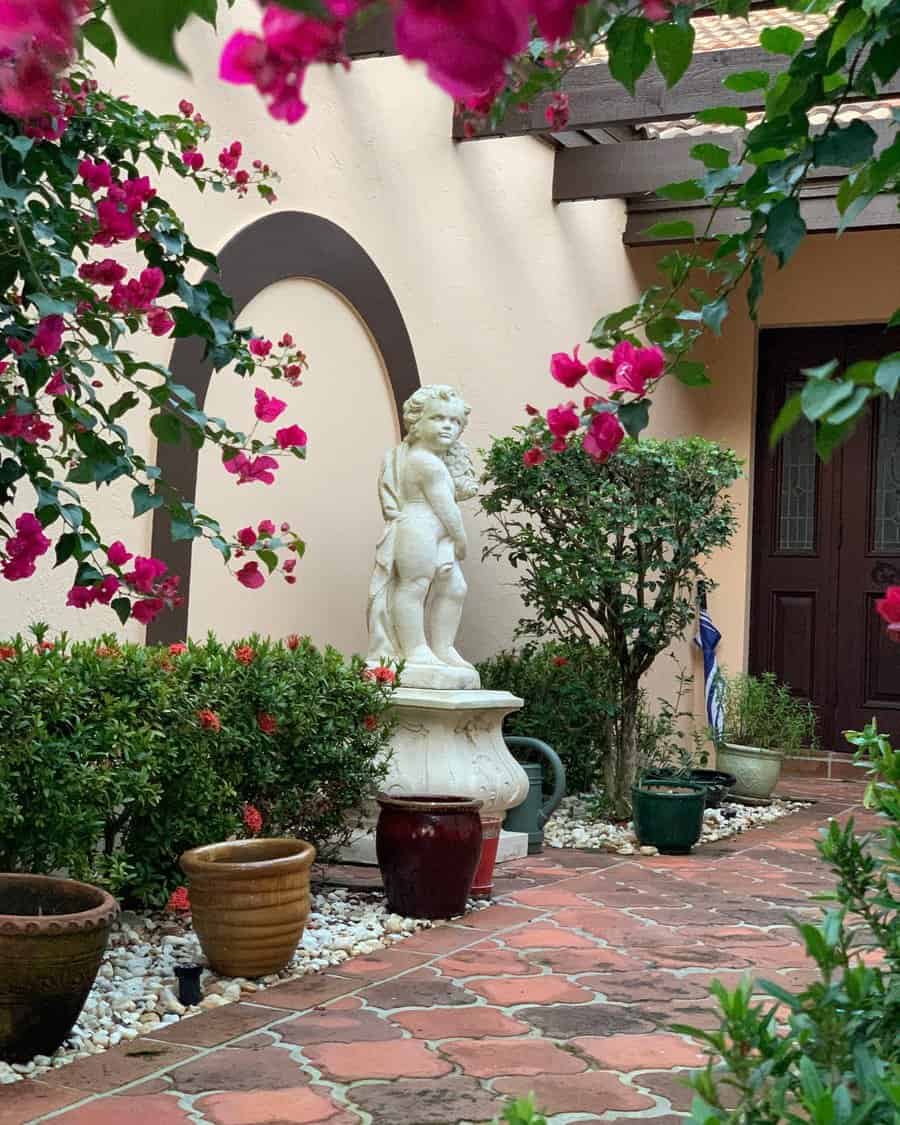 Elegant Mediterranean-style Florida garden with terracotta tiles, a classical cherub statue, vibrant bougainvillea, and lush greenery for a timeless courtyard charm