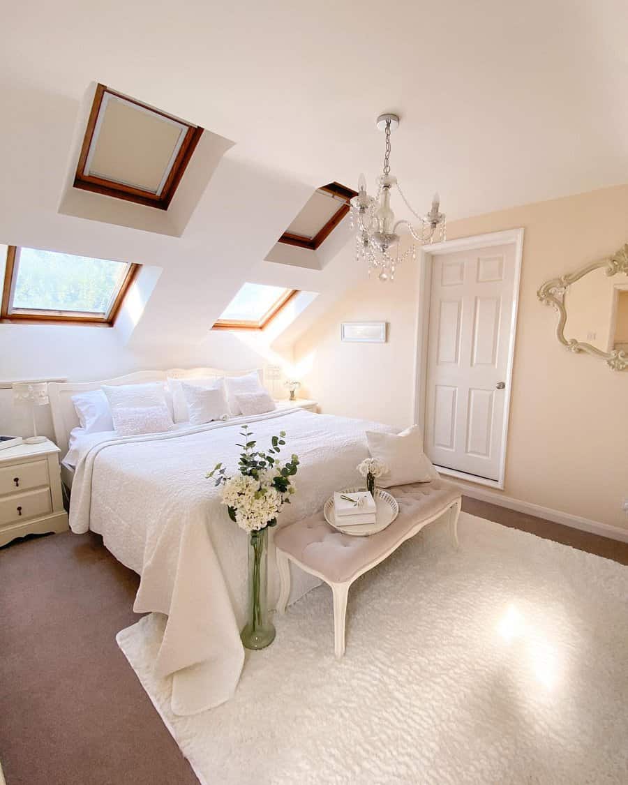 Elegant attic bedroom with skylights, a crystal chandelier, and soft neutral tones. Plush textures and vintage decor create a luxurious retreat.