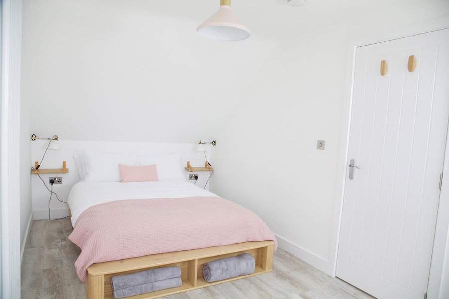 Minimalist attic bedroom with a soft pink and white palette, built-in bed storage, and floating shelves. A cozy and functional small-space retreat.