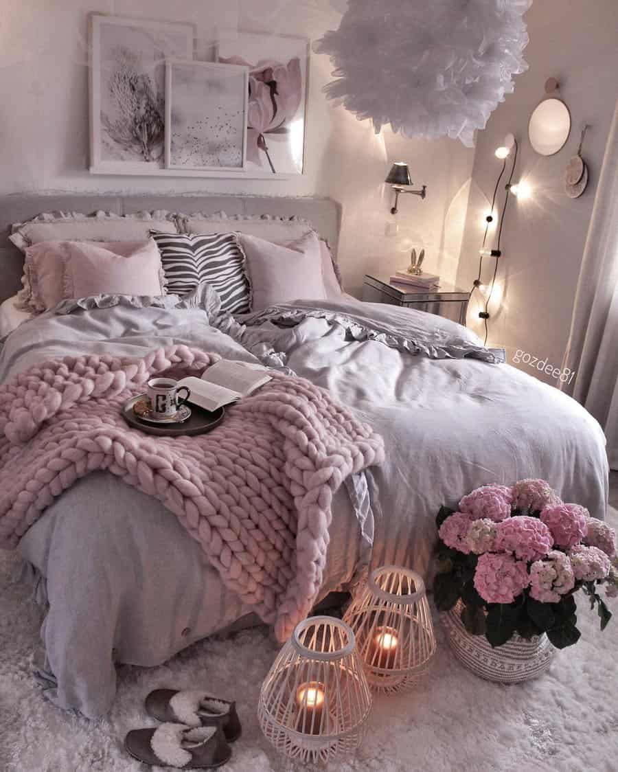 Glam bedroom with a pink knit blanket, framed art, and floral decor. Lanterns with candles and hydrangeas add warmth to the soft lighting