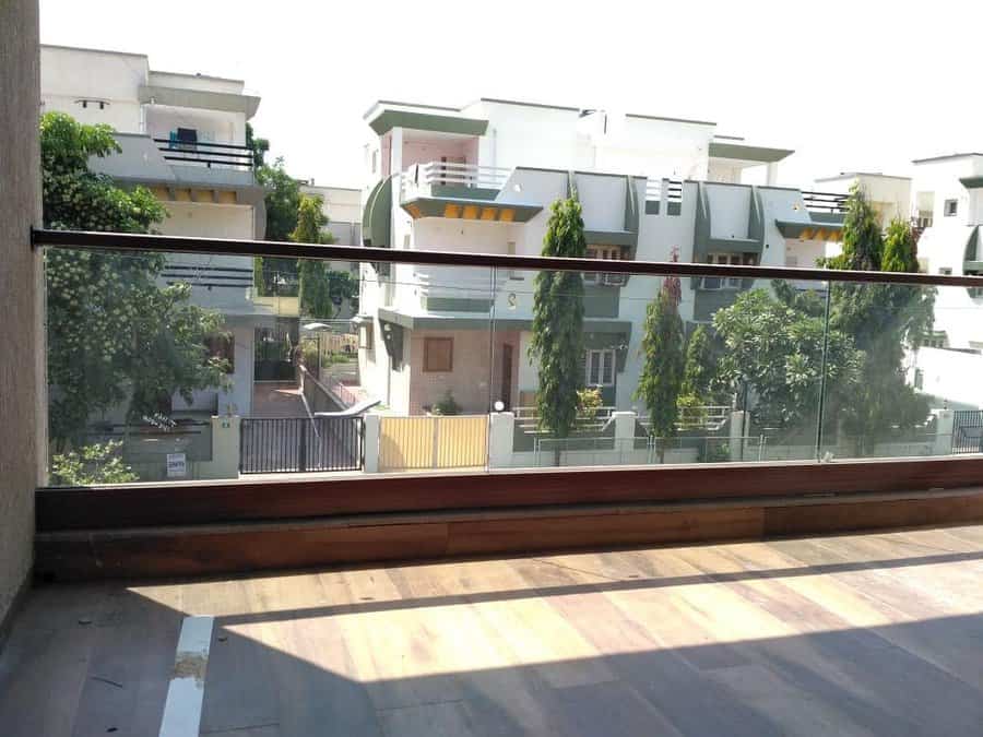 Minimalist balcony with a sleek glass railing and wooden flooring, offering an open and unobstructed view of a modern residential neighborhood