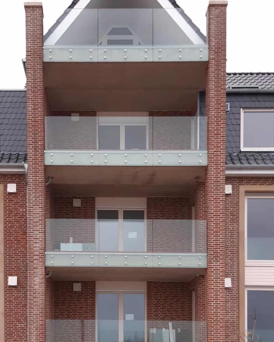 A modern brick apartment building with four glass-fronted balconies stacked vertically