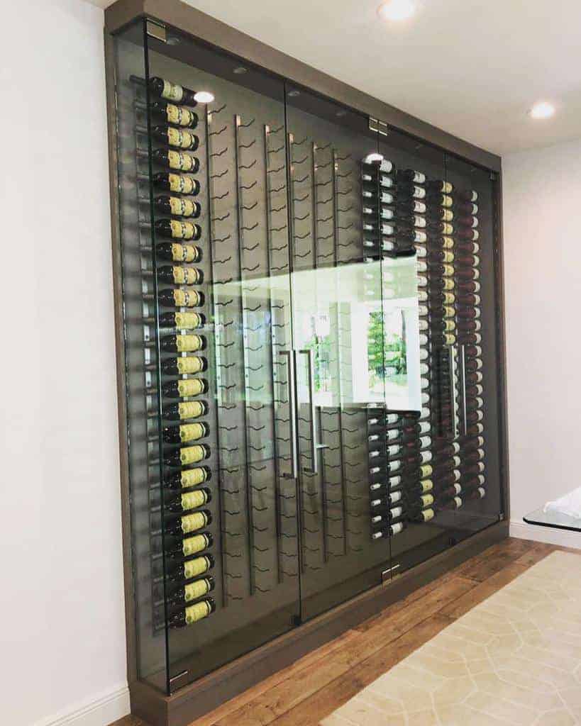 A modern glass wine rack filled with rows of wine bottles in a well-lit room