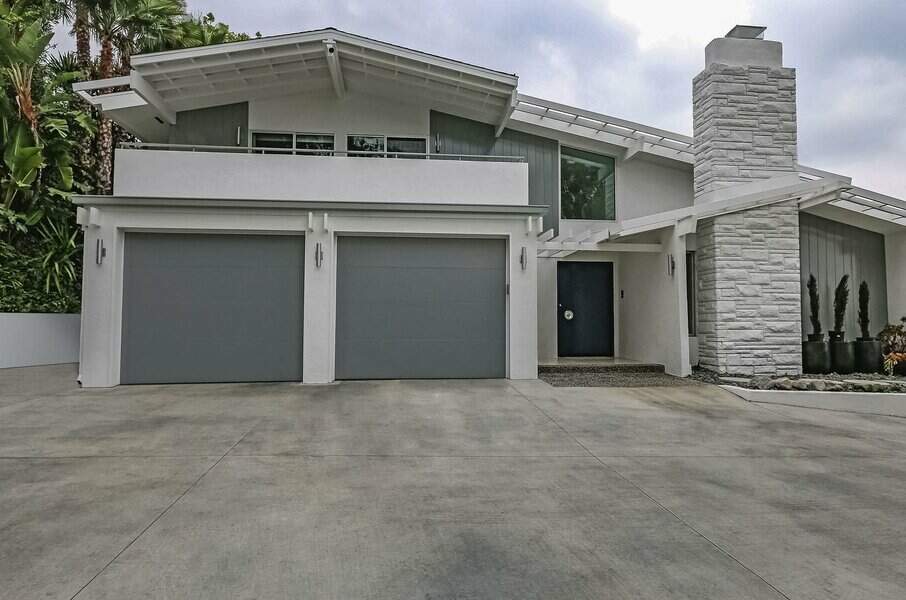 Modern white home with two gray garage doors and lush greenery