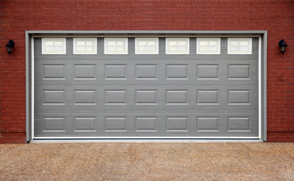 Gray garage door on a red brick house with wall lanterns