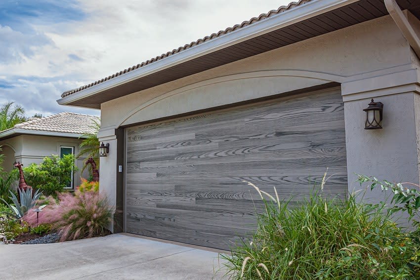 House with textured grey garage door and tropical landscaping