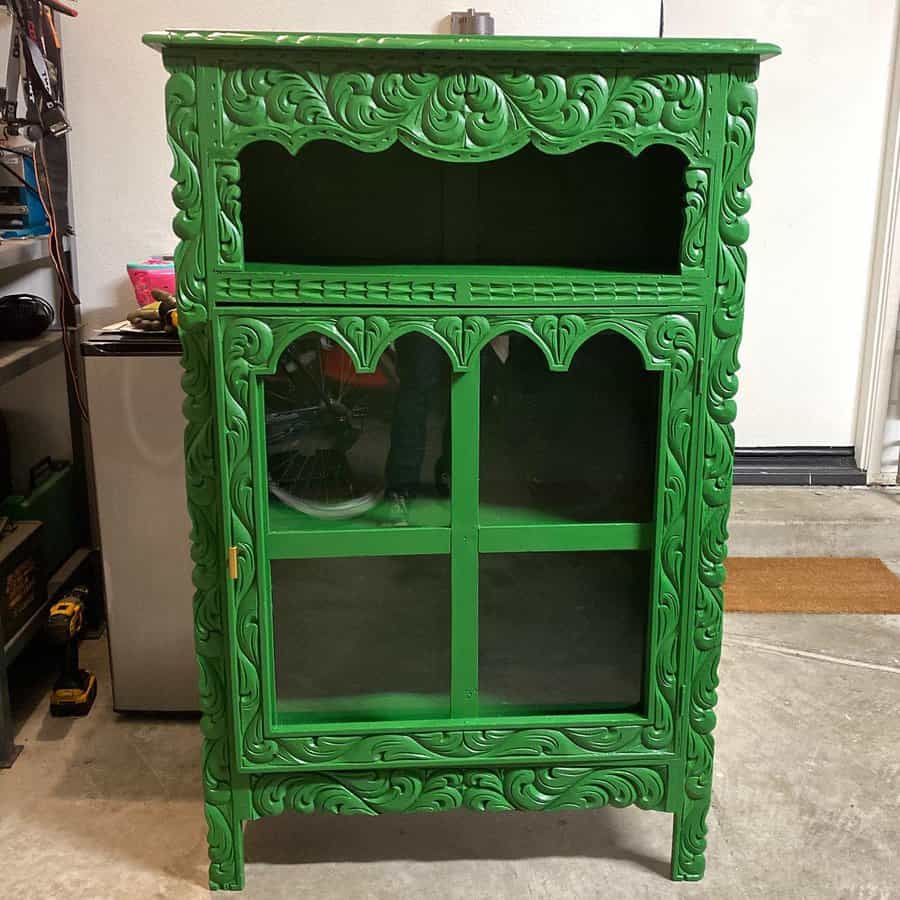 Intricately carved wooden cabinet painted in bold green, featuring glass doors and ornate detailing for a striking vintage look.