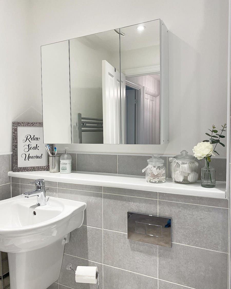 Clean and modern bathroom with grey tile backsplash, mirrored cabinet, white sink, and minimal decor for a fresh, relaxing vibe.