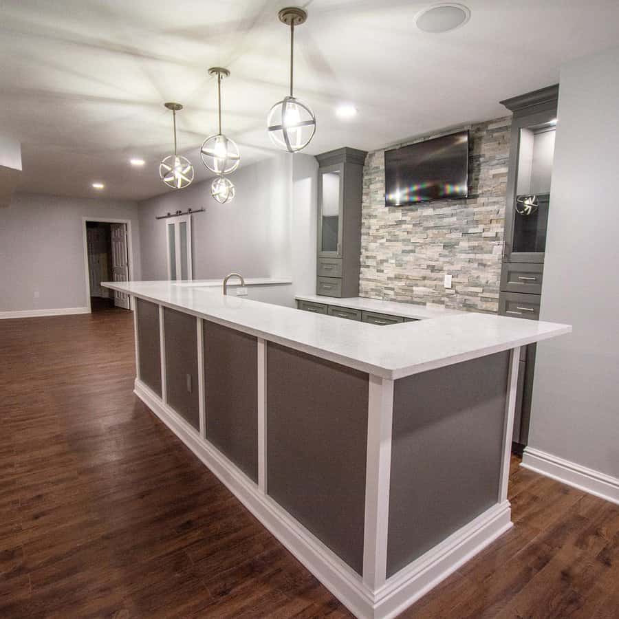 Modern basement bar with a sleek grey and white design, stone accent wall, pendant lighting, and built-in cabinetry for a stylish entertainment space.