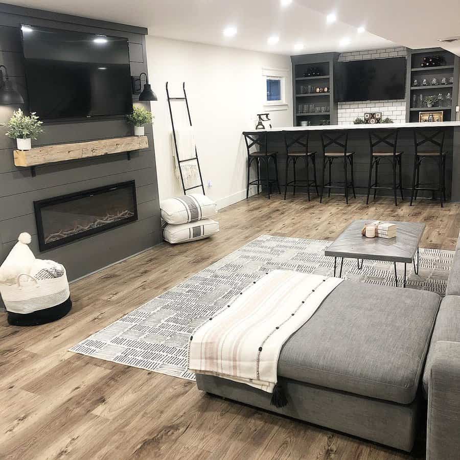 Stylish basement with a cozy lounge, modern fireplace, grey bar seating, and wood accents for a warm and inviting entertainment space.