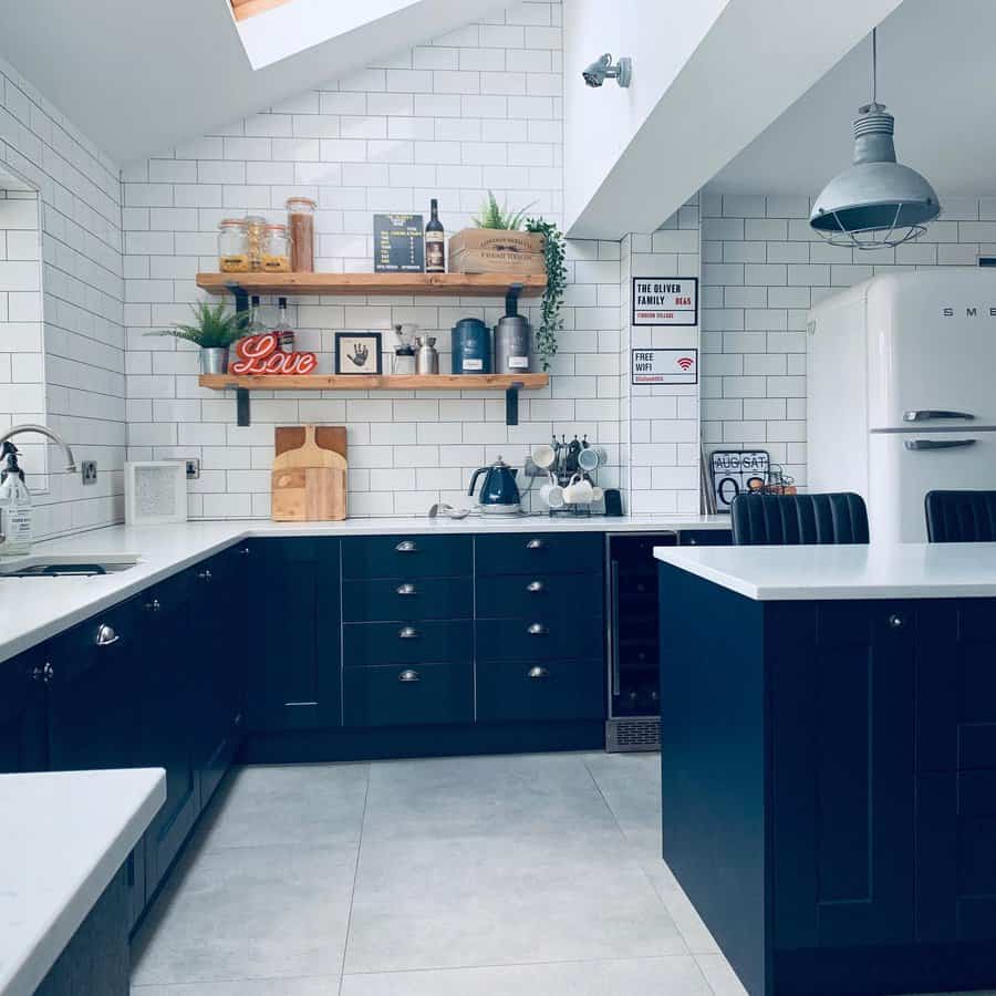 Light grey tile flooring enhances this modern kitchen, complementing navy cabinetry, white subway tiles, and open wooden shelving for a stylish look