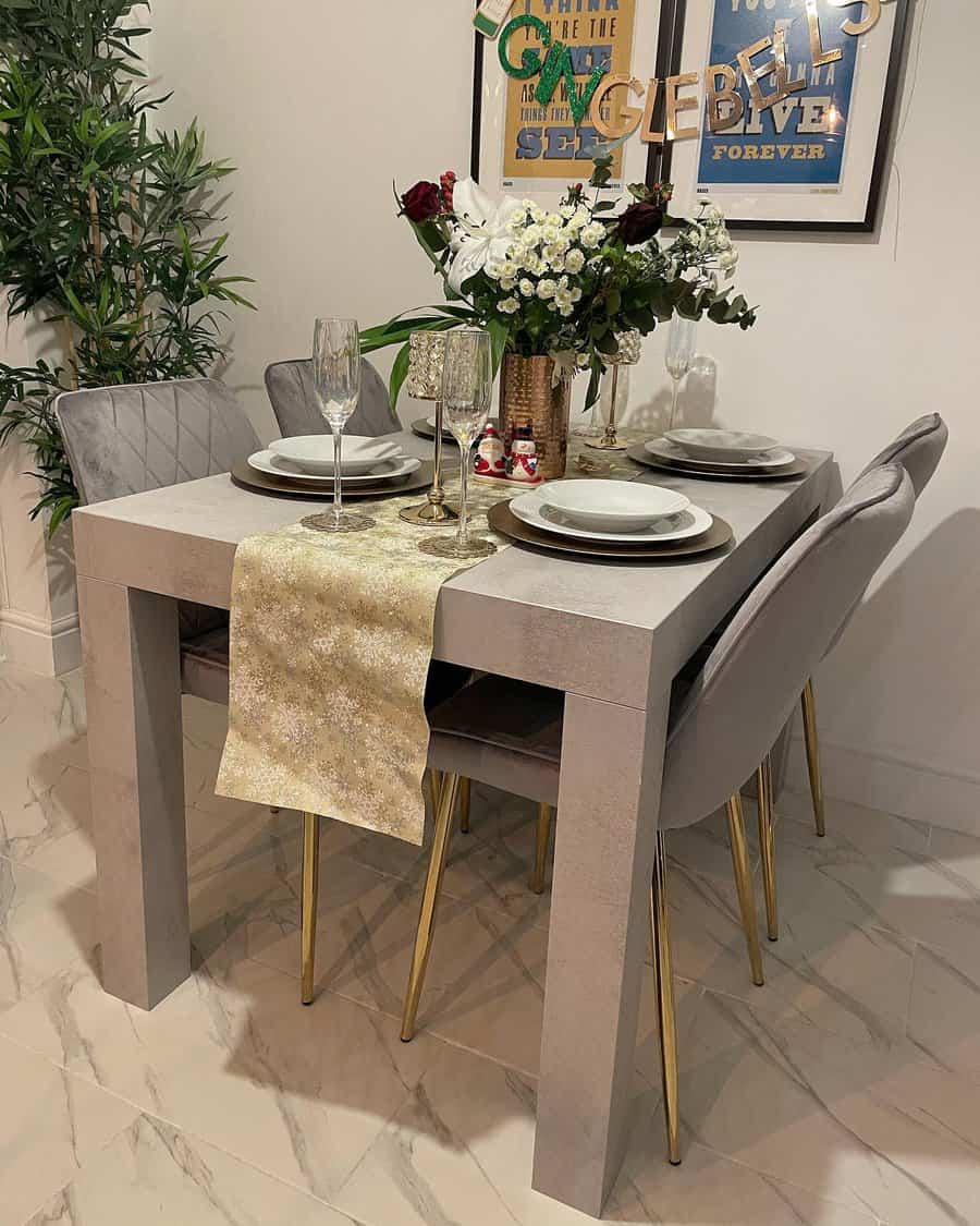 Elegant dining table set with four chairs, a flower centerpiece, wine glasses, plates, and a gold table runner in a cozy setting