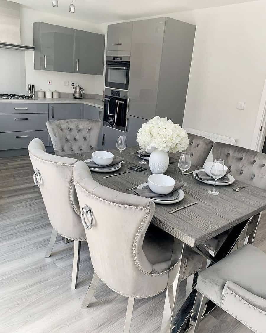 Modern kitchen with gray cabinets, stainless appliances, and a dining table set with gray velvet chairs and white floral centerpiece