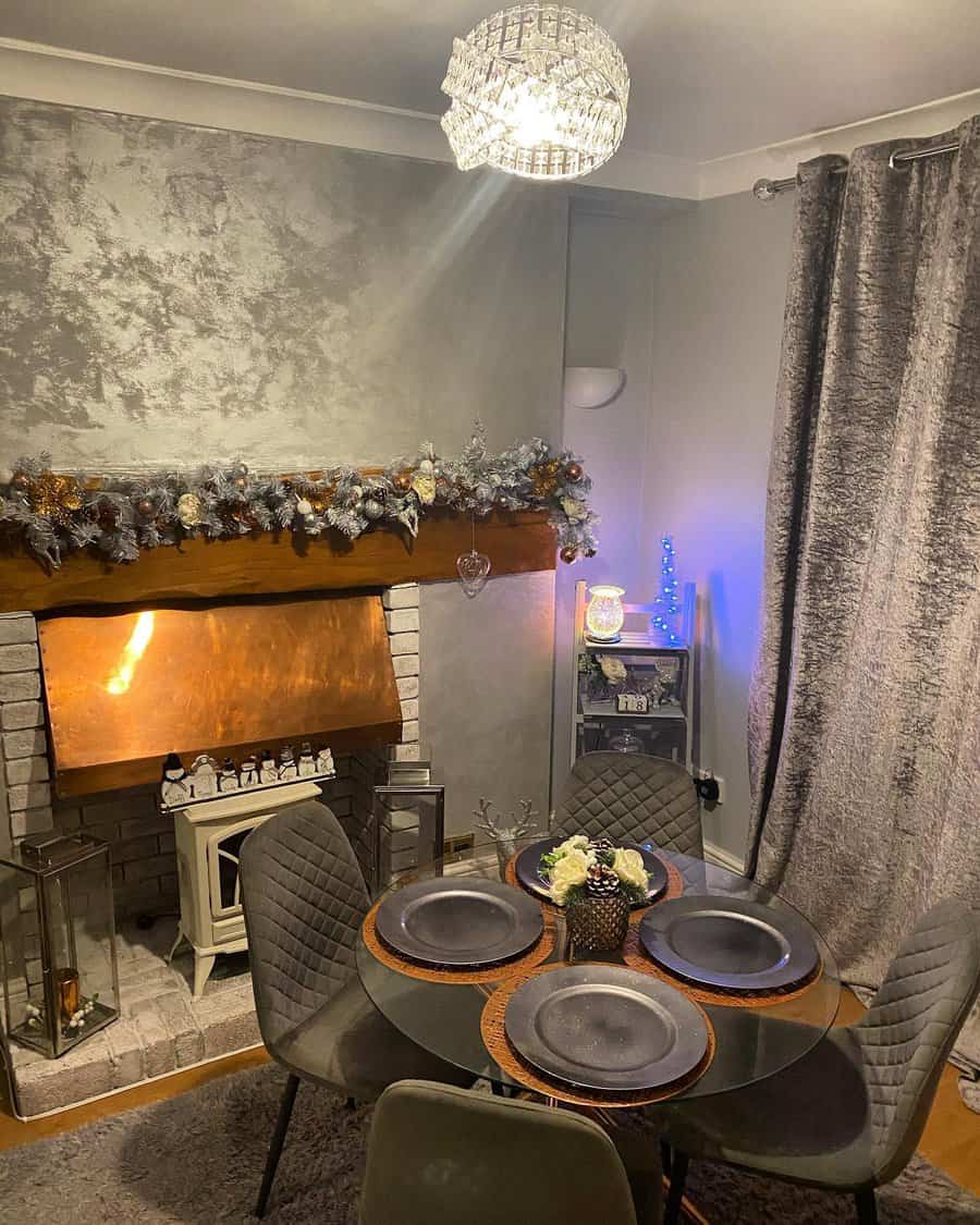 Cozy dining room with a decorated fireplace, chandelier, and table set for four in silver and gray tones