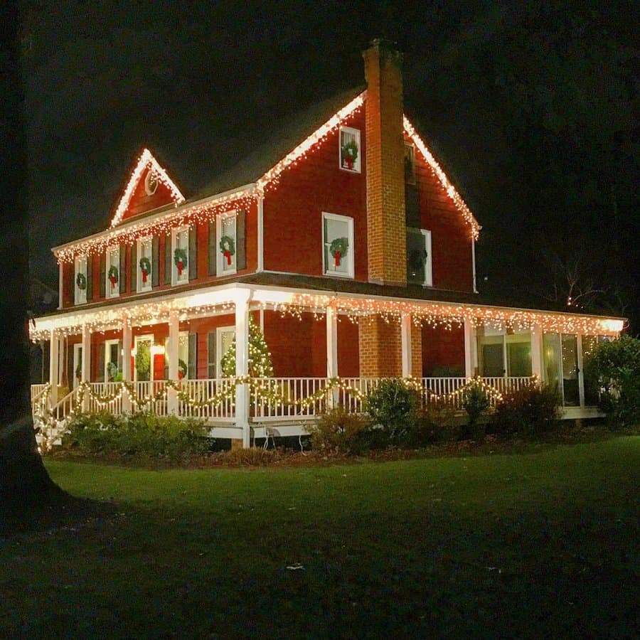 A large red house with Christmas lights and wreaths on the porch and roof, glowing warmly against the night sky