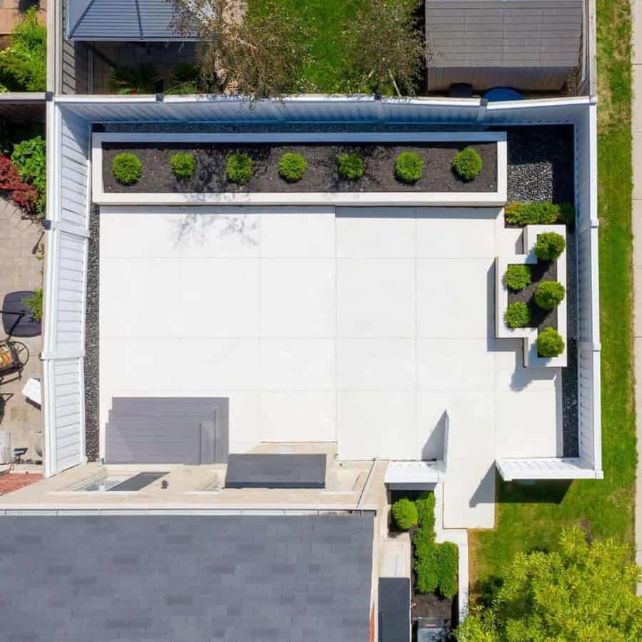 Aerial view of a modern backyard with clean white concrete paving, raised planters, and neatly trimmed greenery for a minimalist design