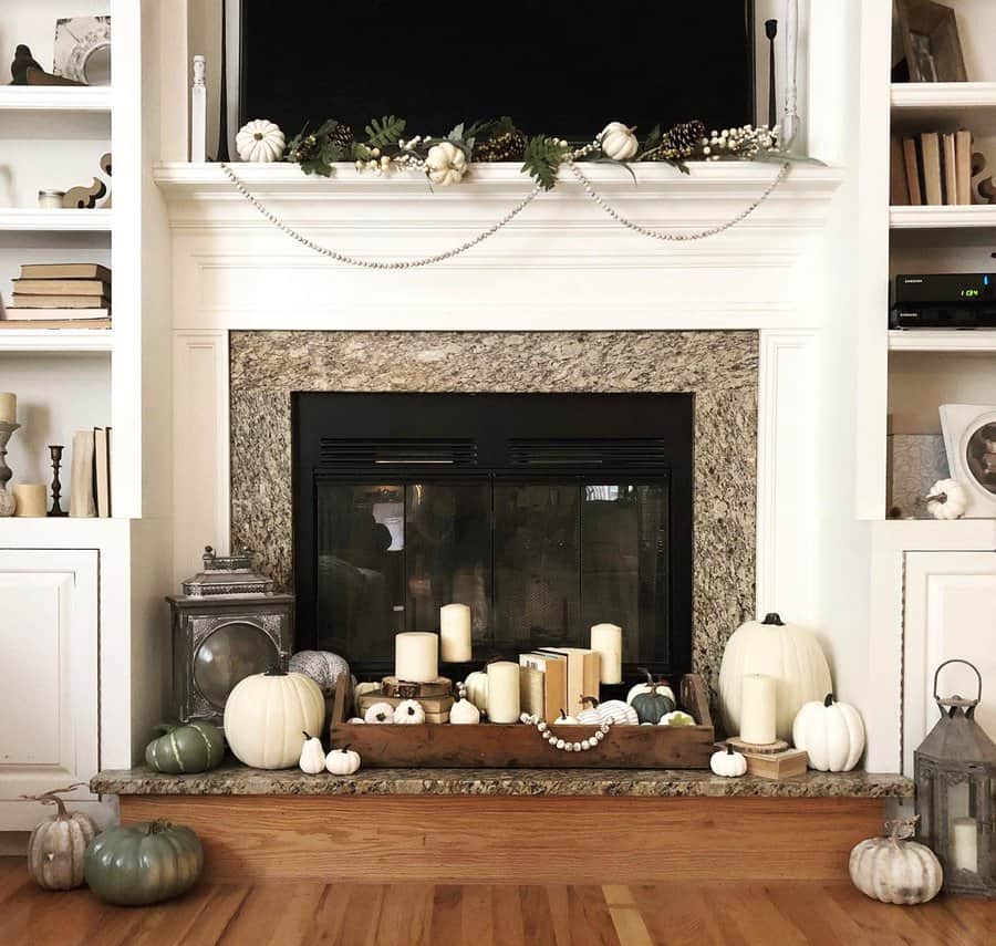 Cozy fireplace decorated with white pumpkins, candles, and greenery, surrounded by books and lanterns on a wooden floor