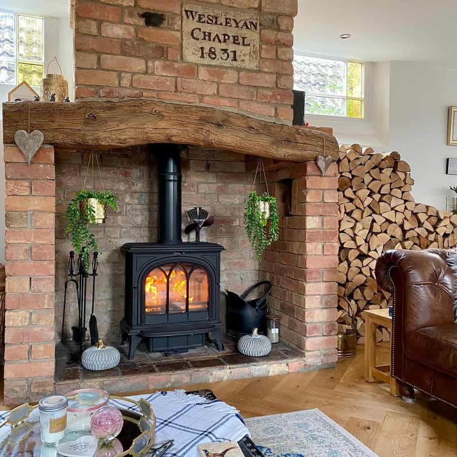 Cozy living room with a wood-burning stove in a brick fireplace, surrounded by stacked logs. A rustic sign reads "Wesleyan Chapel 1831"