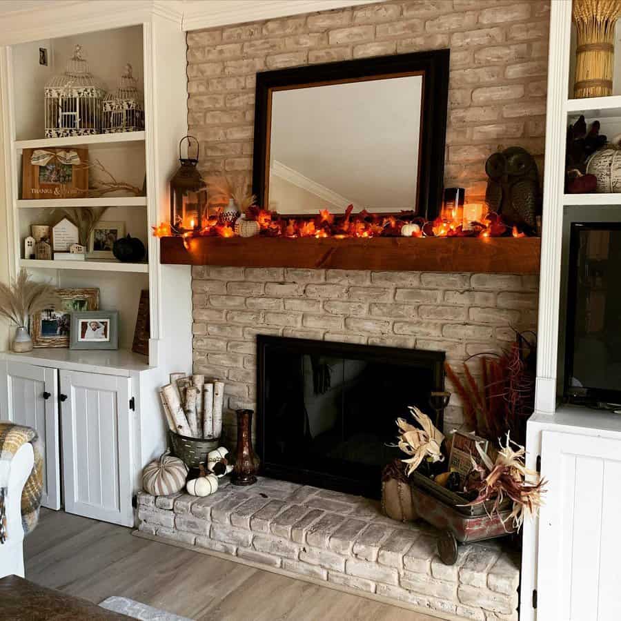 Cozy living room with a brick fireplace decorated with autumn leaves, pumpkins, and candles, bookshelves on the sides with various decor items