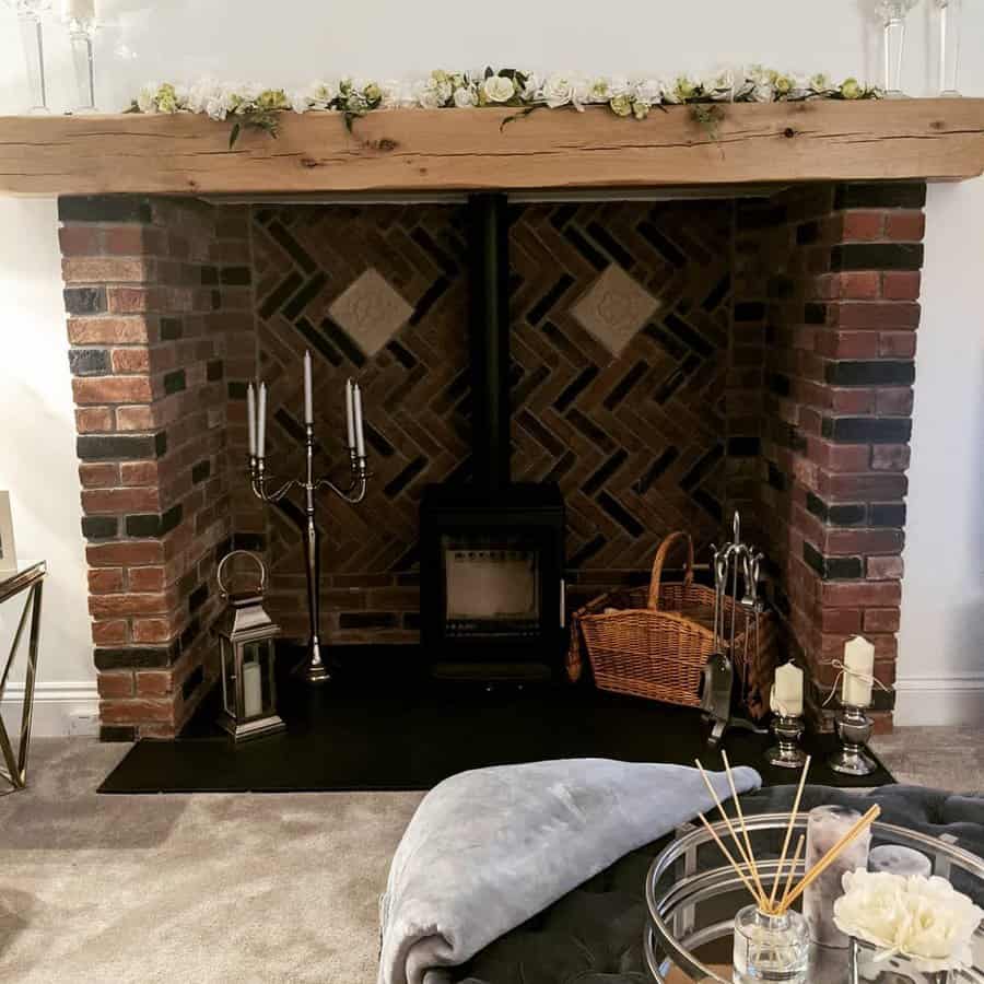 Cozy living room with brick fireplace, wood-burning stove, candle holders, basket, and floral mantel decoration