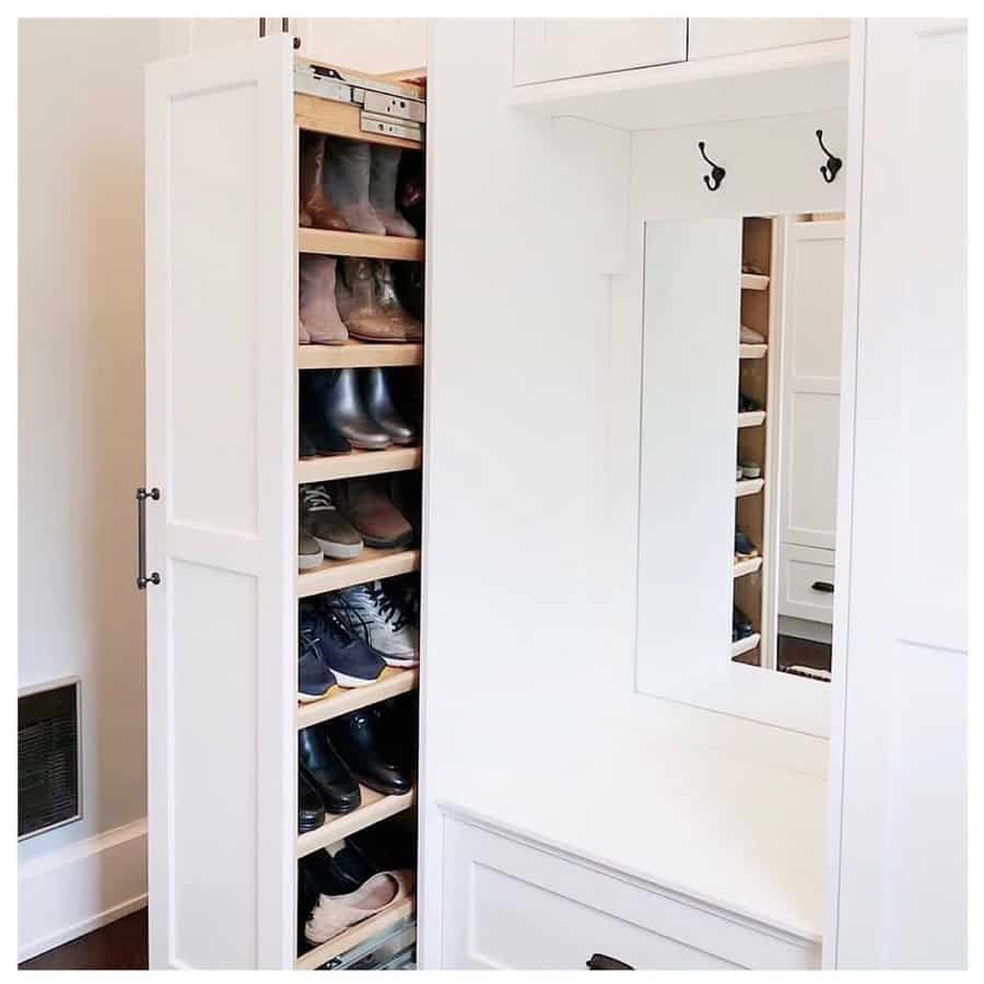 White closet with a pull-out shoe rack filled with various shoes next to a wall mirror and hooks