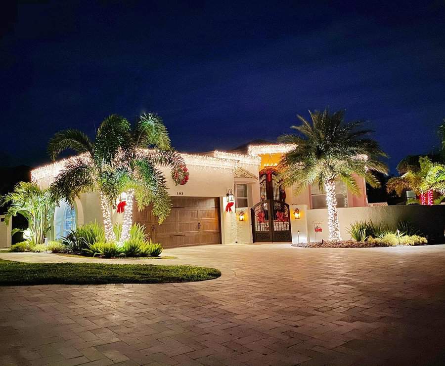 Single-story house with palm trees, decorated with white holiday lights at night