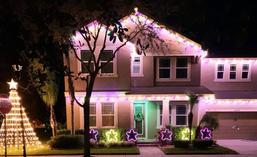 House at night with colorful Christmas lights outlining the roof and windows, and star-shaped lights on the lawn