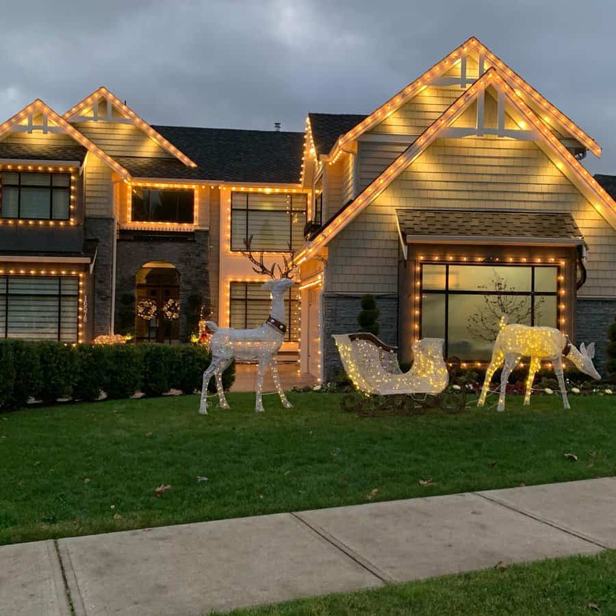 House adorned with Christmas lights, featuring illuminated reindeer and a sleigh on the lawn with a cloudy evening sky in the background