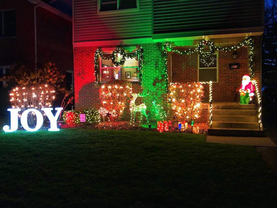 House decorated with colorful Christmas lights, featuring a lit "JOY" sign and Santa figure on the steps