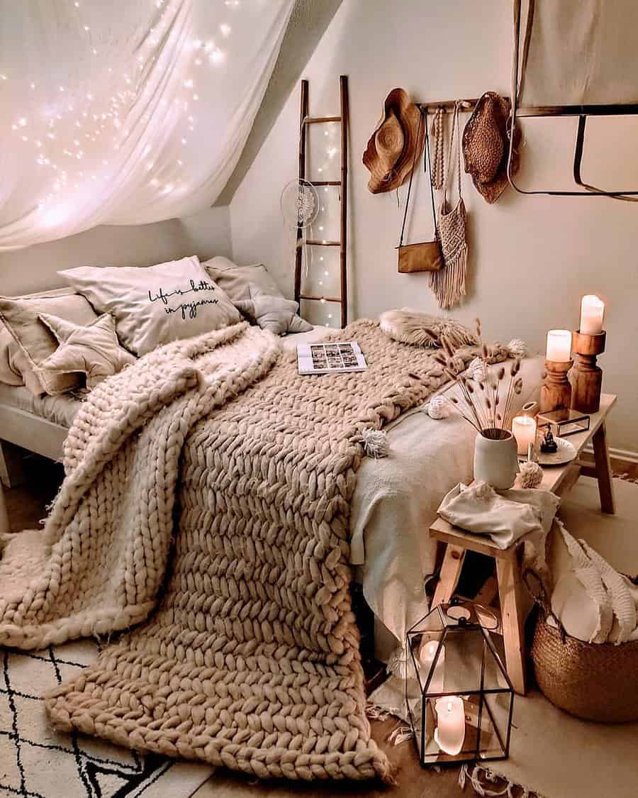 Cozy bedroom with a chunky knit blanket, lit candles, a rustic ladder, hats on the wall, and soft lighting from fairy lights