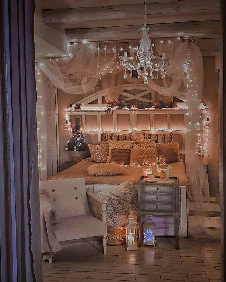 Cozy bedroom with a canopy bed, string lights, a chandelier, and rustic decor. A side table with candles and a chair are nearby