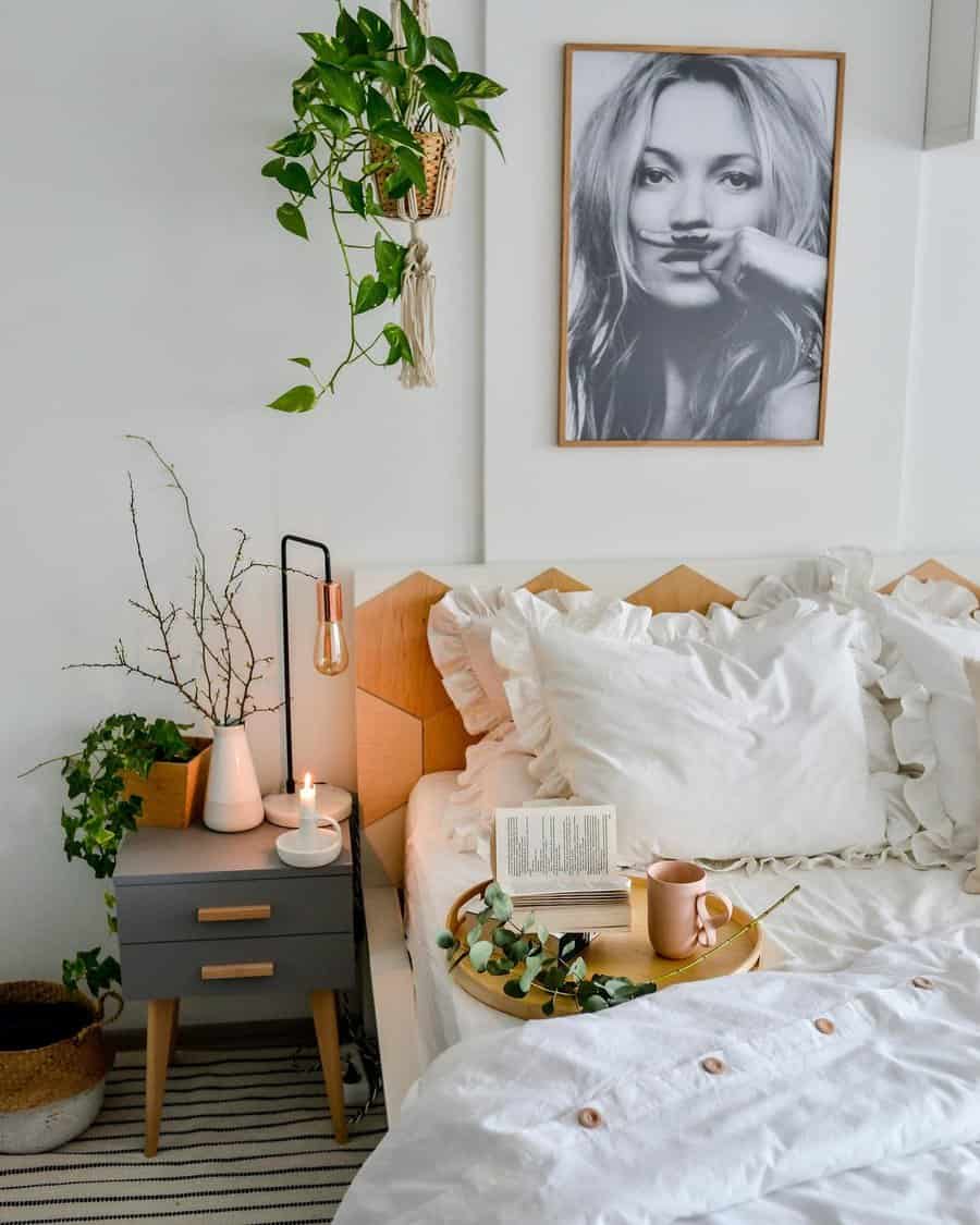 Small bedroom with a bed, white bedding, a bedside table with a plant, lamp, book, and a framed photo on the wall above