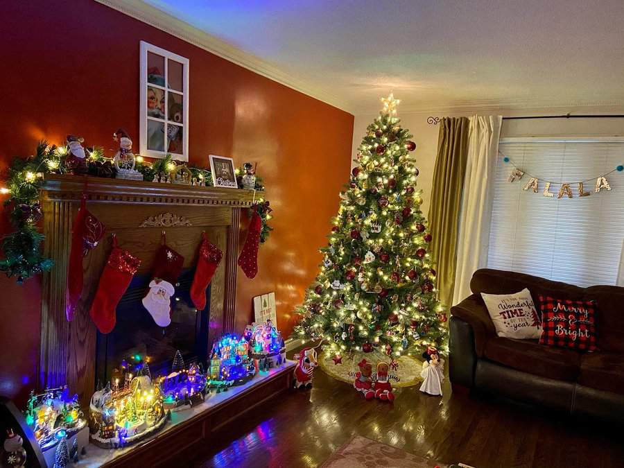 A cozy living room decorated for Christmas with a lit tree, stockings on the mantel, and festive lights illuminating the space