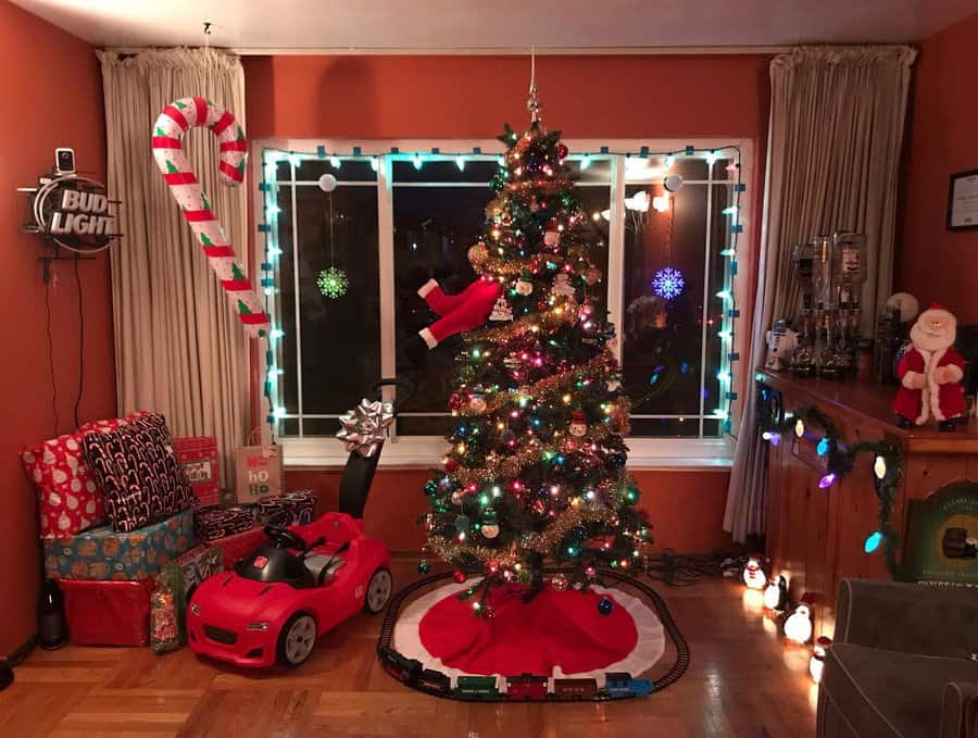 A festive living room with a decorated Christmas tree, Santa decor, wrapped gifts, and a toy car, candy cane lights adorn the window