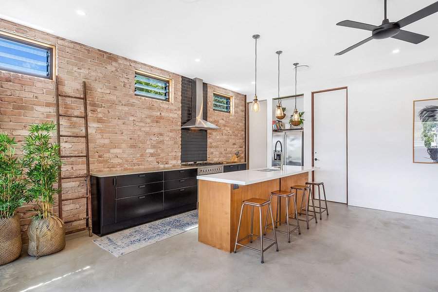 Modern industrial kitchen with an exposed brick wall, sleek black cabinetry, a wooden island breakfast bar, metal barstools, and pendant lighting