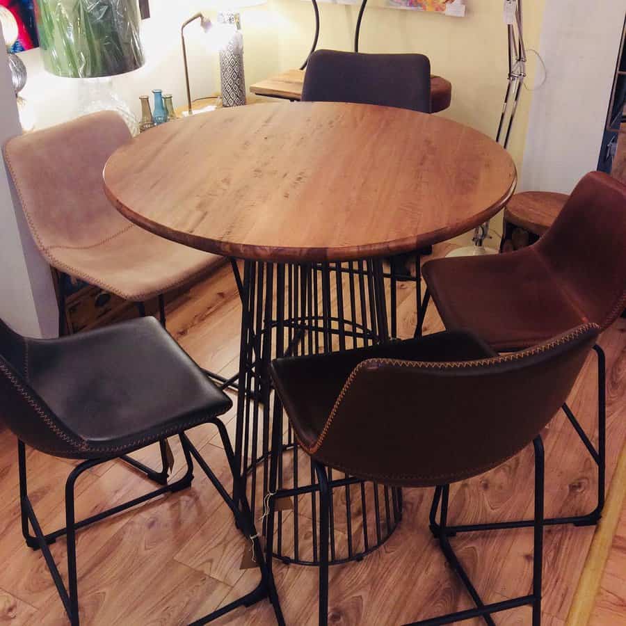 Round wooden table with a metal base, surrounded by four leather chairs on a wooden floor