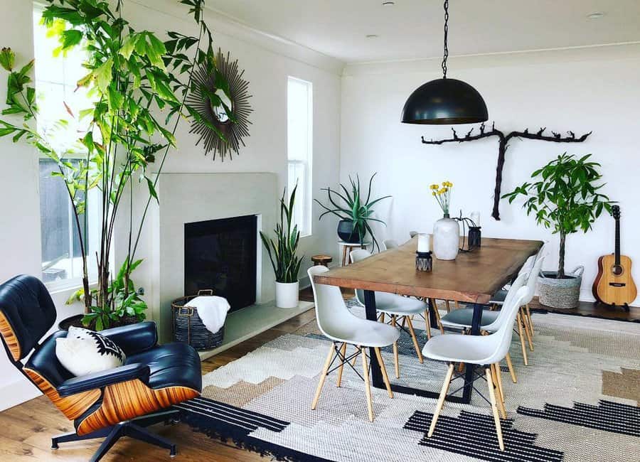 Modern living room with a wooden dining table, white chairs, plants, a fireplace, a stylish chair, wall art, and a guitar