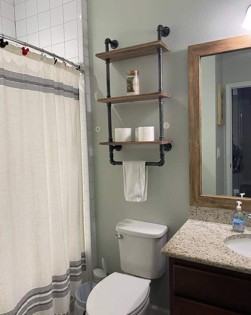 Industrial-style floating shelves with black pipe supports hold toiletries and toilet paper above a toilet in a modern farmhouse bathroom