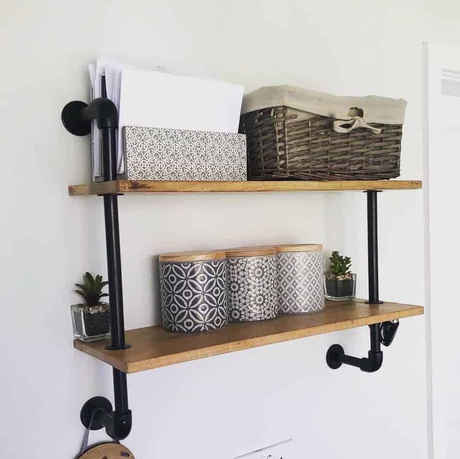 Wall-mounted wooden shelves with black metal brackets, holding a woven basket, documents, decorative tins, and small potted plants