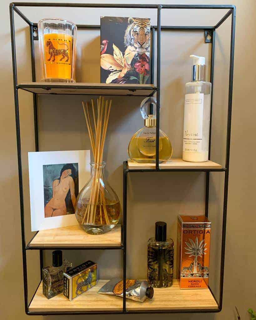 Wall-mounted shelf with candles, perfumes, diffuser, decorative boxes, and a small artwork