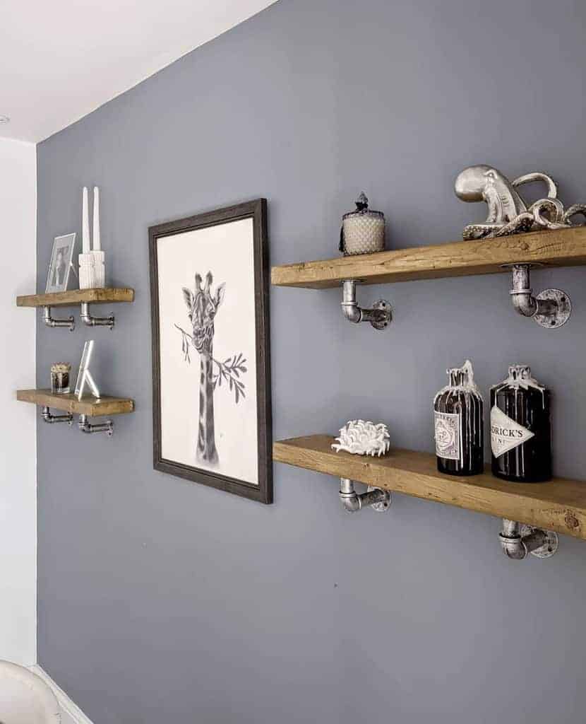 Industrial-style floating shelves with metal pipe brackets on a gray wall, decorated with candles, art, and eclectic decor pieces