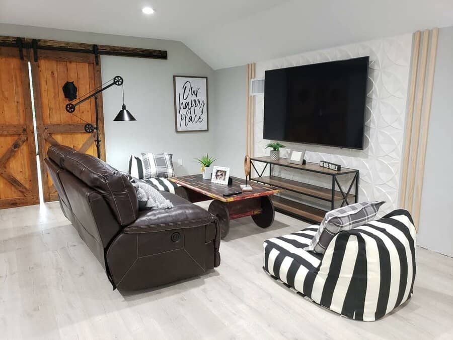 Modern living room with a leather sofa, striped bean bag, wall-mounted TV, barn doors, and decorative wall paneling