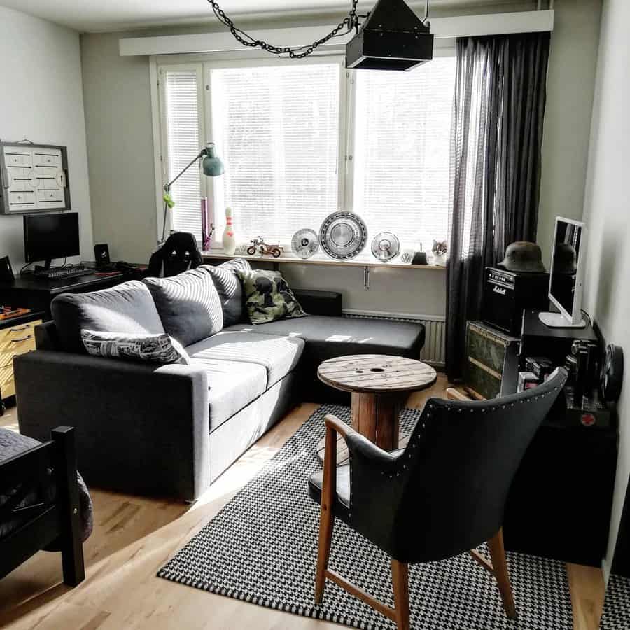 Industrial-style living room with a dark gray sectional, black leather chair, metal accents, a spool coffee table, and a monochrome houndstooth rug