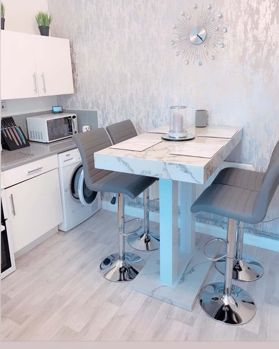 Modern breakfast bar with a marble-style table, sleek grey barstools, metallic accents, and a stylish textured wall for a chic dining space