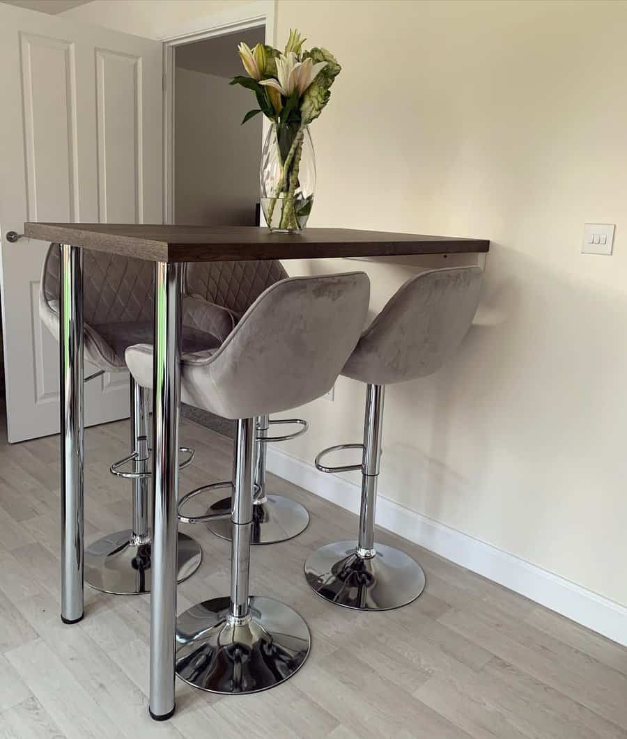 Elegant breakfast bar with a dark wood tabletop, plush grey quilted barstools, chrome legs, and a vase of fresh flowers for a stylish touch