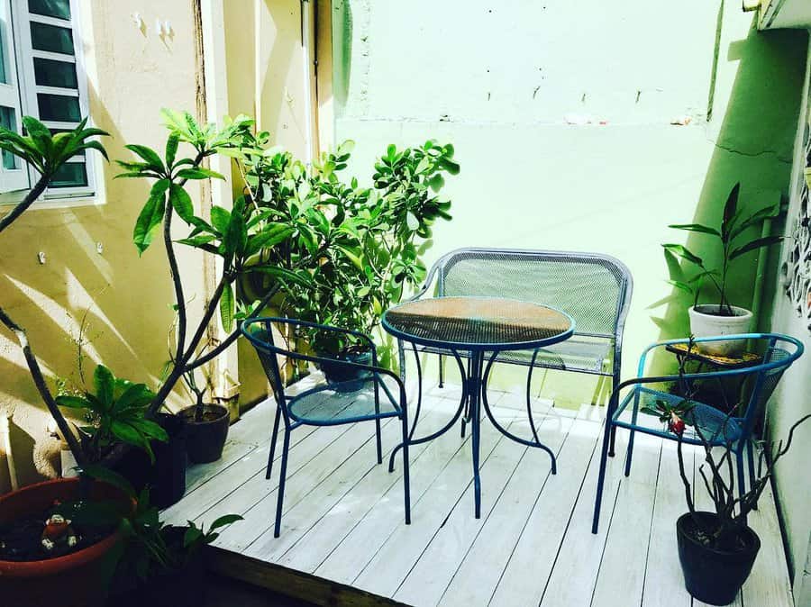 Cozy patio with a small round table, two chairs, and potted plants on a wooden deck in bright sunlight