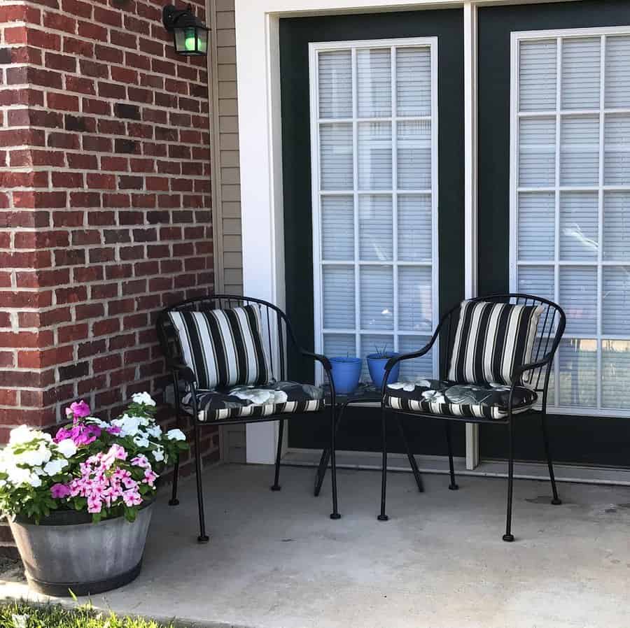 Two striped chairs on a patio beside a brick wall, with a small table holding two blue pots in between and a flower pot on the left